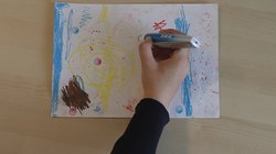 Auf einem Tisch liegt ein Blatt mit Zeichnung, eine Hand mit Audiostift berührt Audiosticker darauf