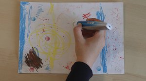 Auf einem Tisch liegt ein Blatt mit Zeichnung, eine Hand mit Audiostift berührt Audiosticker darauf