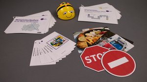 Ein Bee-Bot steht umgeben von diversen Lern-Materialien und Kärtchen.