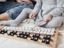 Ein Kind in einem Kleid, dessen Gesicht nicht zu sehen ist, sitzt am Boden und spielt ein Xylophon.
