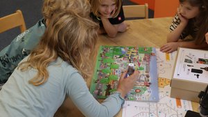 Volksschulkinder sind über ein Wien-Wimmelbuch gebeugt, ein Kind tippt mit einem Audiostift auf das Buch.